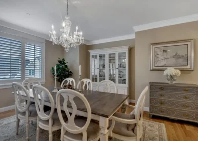 Elegant dining room with chandelier, large wooden table, white chairs, and glass cabinet against beige walls.