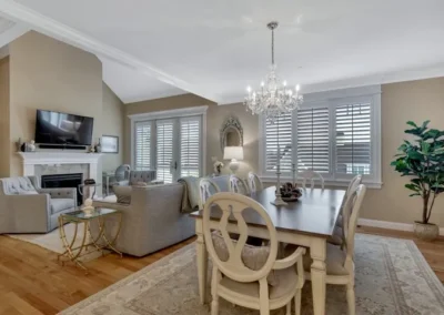 Elegant dining room with chandelier, wooden table, upholstered chairs, and large windows with shutters.