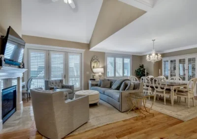 Spacious living room with gray sofas, elegant chandelier, hardwood floors, and large windows with shutters.