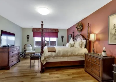 Spacious bedroom with four-poster bed, hardwood floor, red accent wall, and elegant wooden furniture.