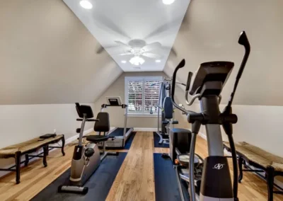 Home gym in attic bedroom with exercise equipment, wooden floor, ceiling fan, and window blinds.