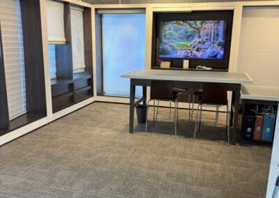 Consultation room with modern table, chairs, large screen displaying nature scene, surrounded by window blinds.