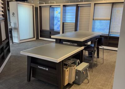 Consultation table in modern showroom with window blinds and overhead lighting fixtures.
