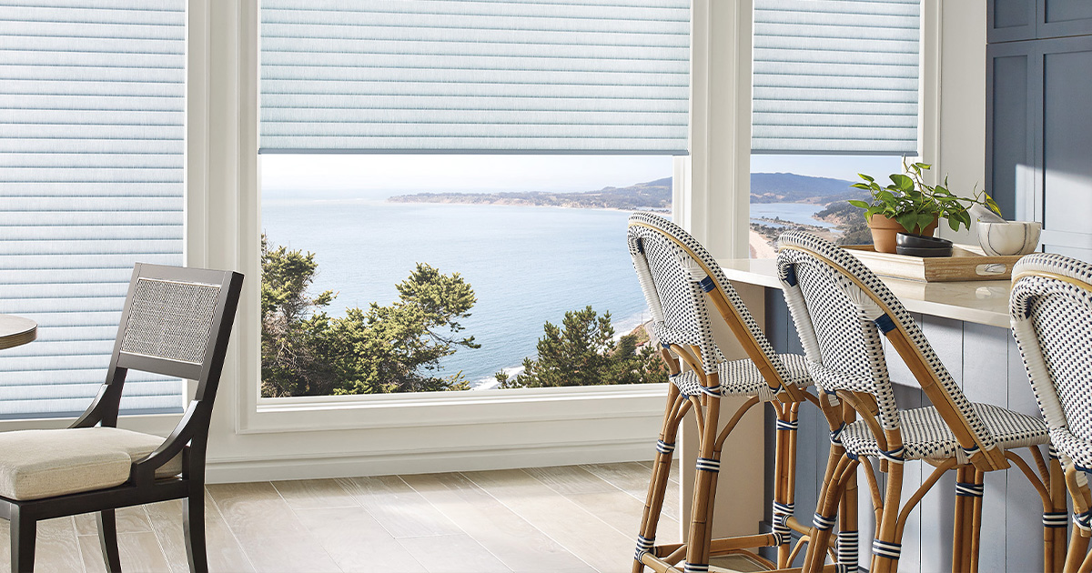 Coastal view through large windows with wicker chairs and potted plant on kitchen counter.